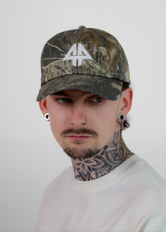 A man wearing a camouflage baseball cap with a white stylized '44' logo on the front, photographed against a plain light gray background.