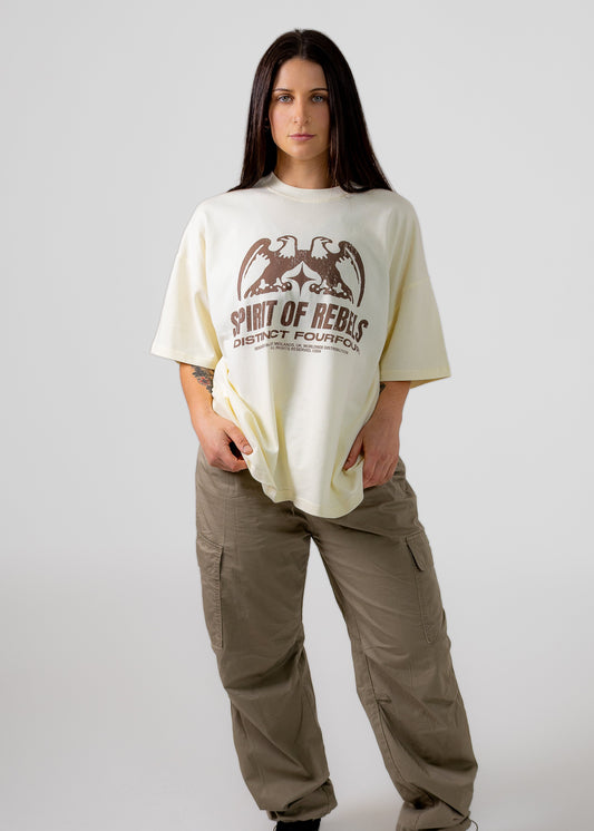 Person wearing a cream t-shirt with a graphic design and text, standing against a plain background