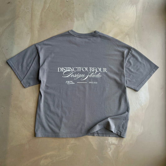 Pigment Grey t-shirt with white text on a concrete surface