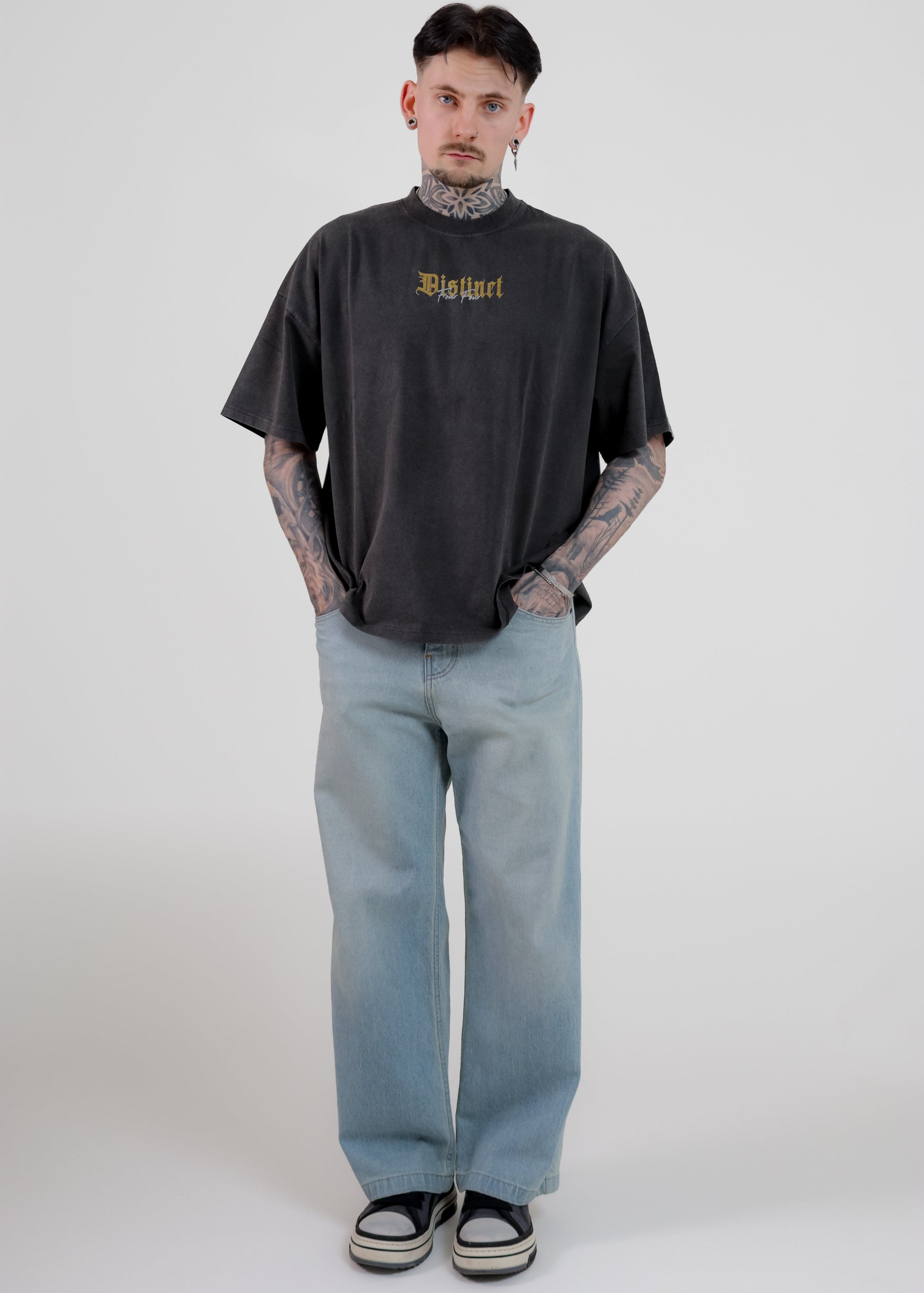 Person wearing a black oversized t-shirt with text and light blue jeans on a white background