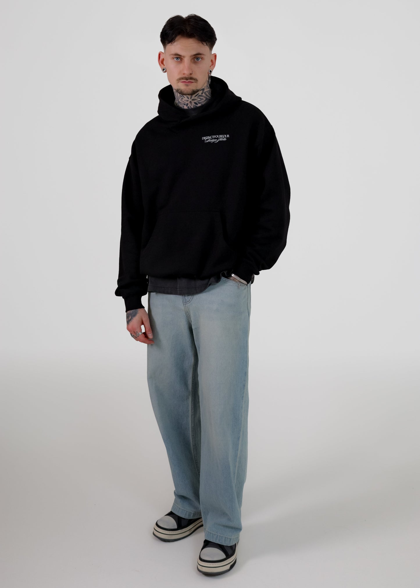 Man wearing a black hoodie and light blue jeans on a white background