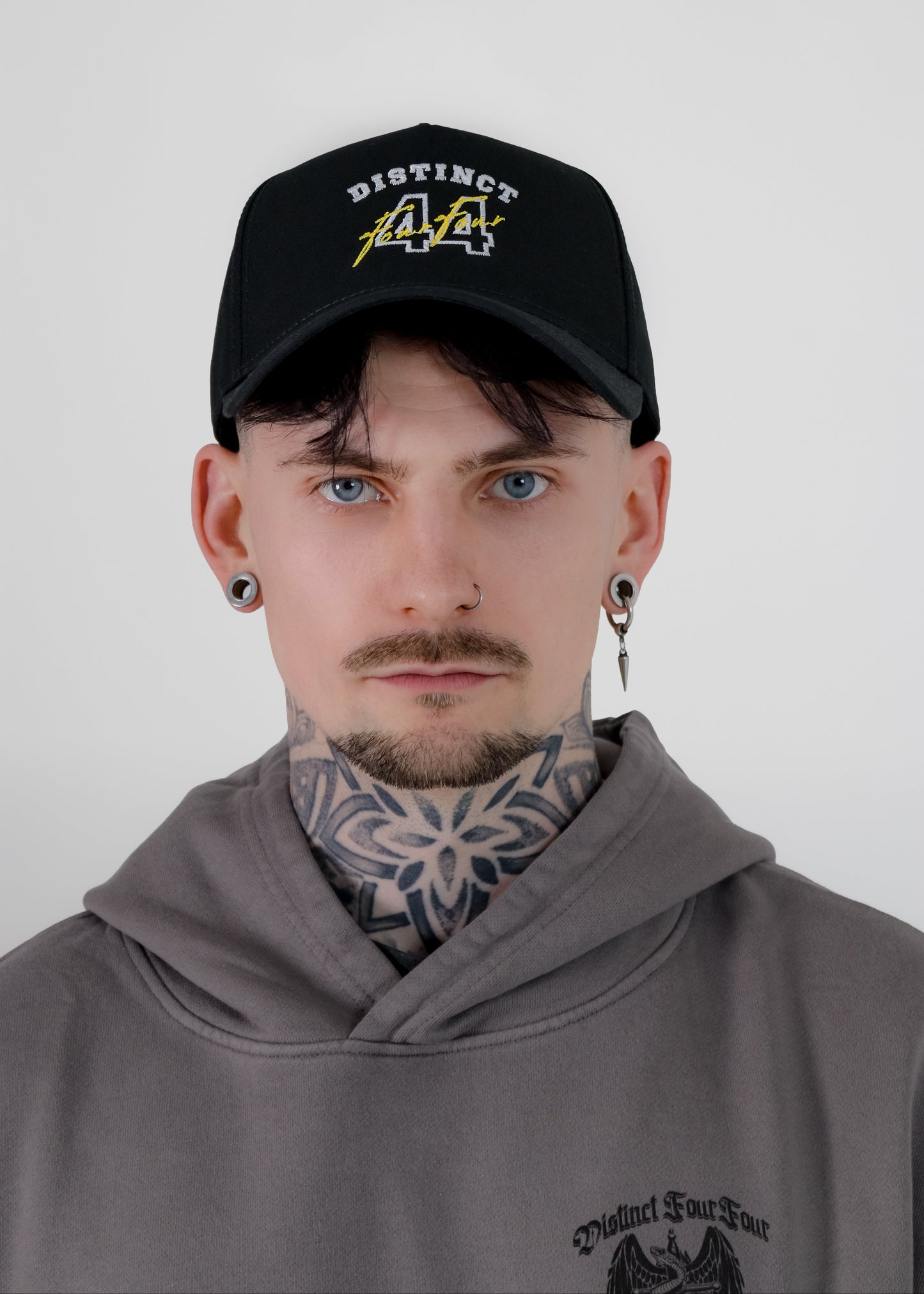 Person wearing a black cap with text and a gray hoodie on a plain background