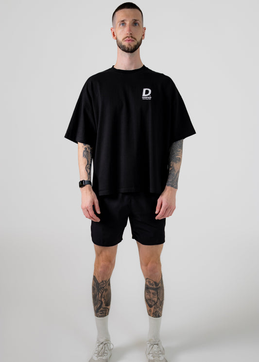 Man wearing a black t-shirt with a logo and black shorts on a white background