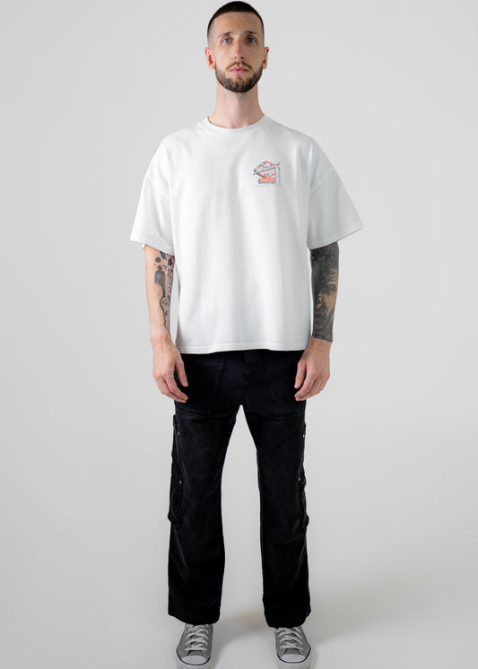 Man wearing a white t-shirt with a small graphic and black pants on a plain background