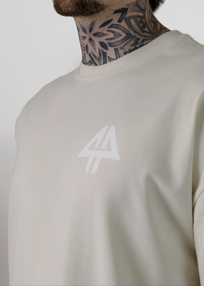 A close-up of a man wearing a light beige crewneck sweatshirt with a white logo on the chest, set against a plain light grey background.