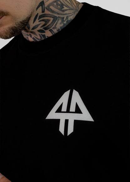 A close-up of a person wearing a black crewneck t-shirt with a white stylized geometric logo on the chest, set against a plain light gray background.