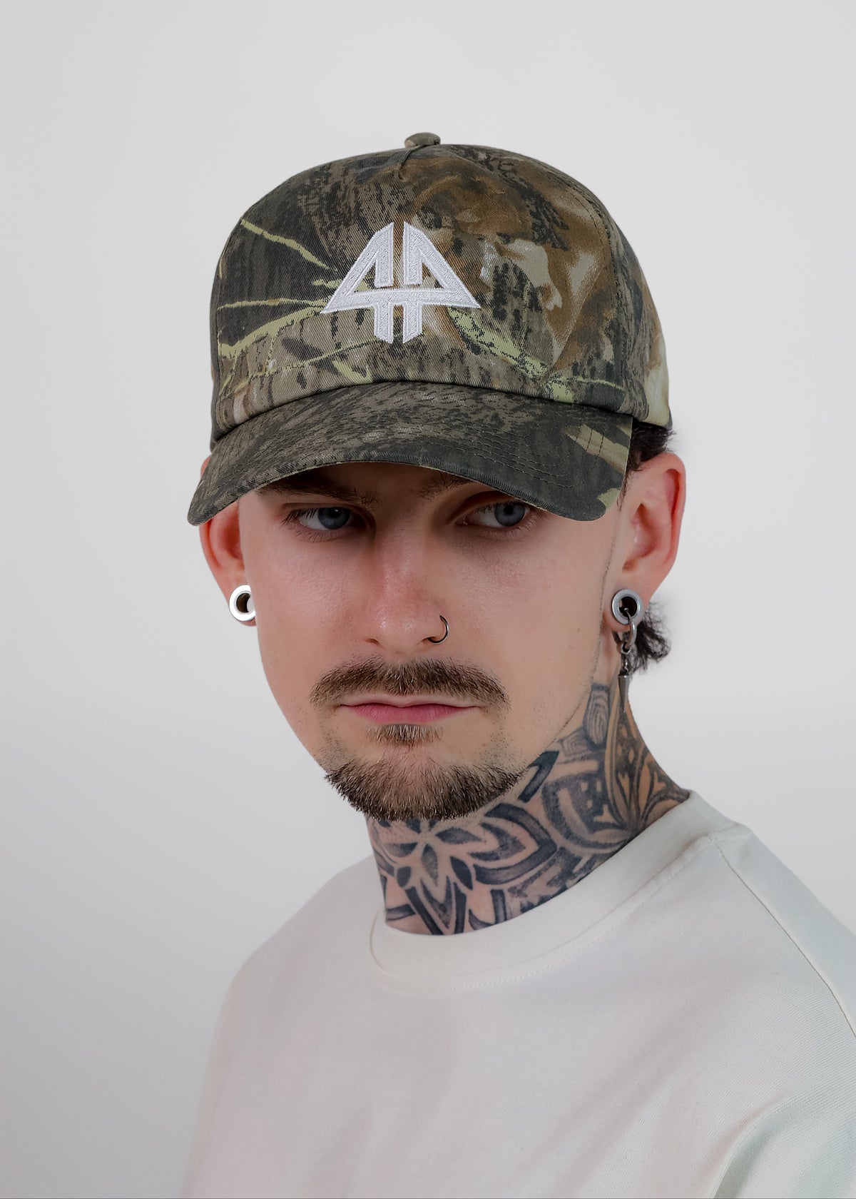 A man wearing a camouflage baseball cap with a white stylized '44' logo on the front, photographed against a plain light gray background.