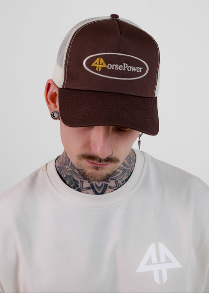 A man wearing a brown and off-white trucker hat with an 'HorsePower' logo patch on the front, paired with a white t-shirt against a light grey background.