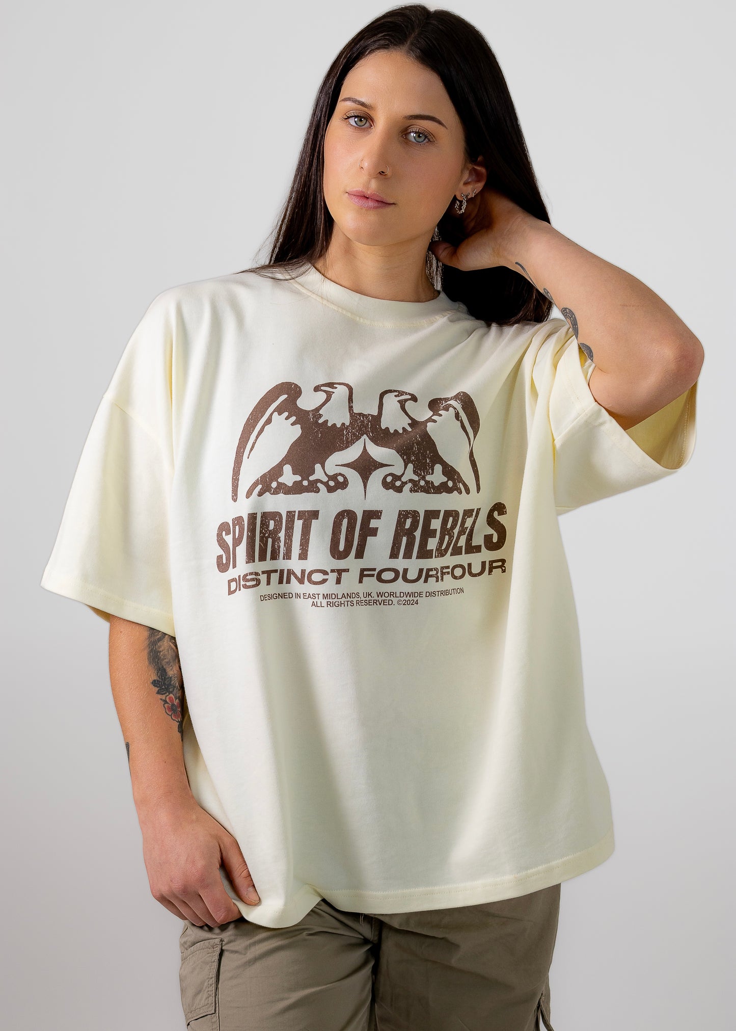 A female model wearing a cream t-shirt with a graphic of an eagle and the text 'SPIRIT OF REBELS' on the front.