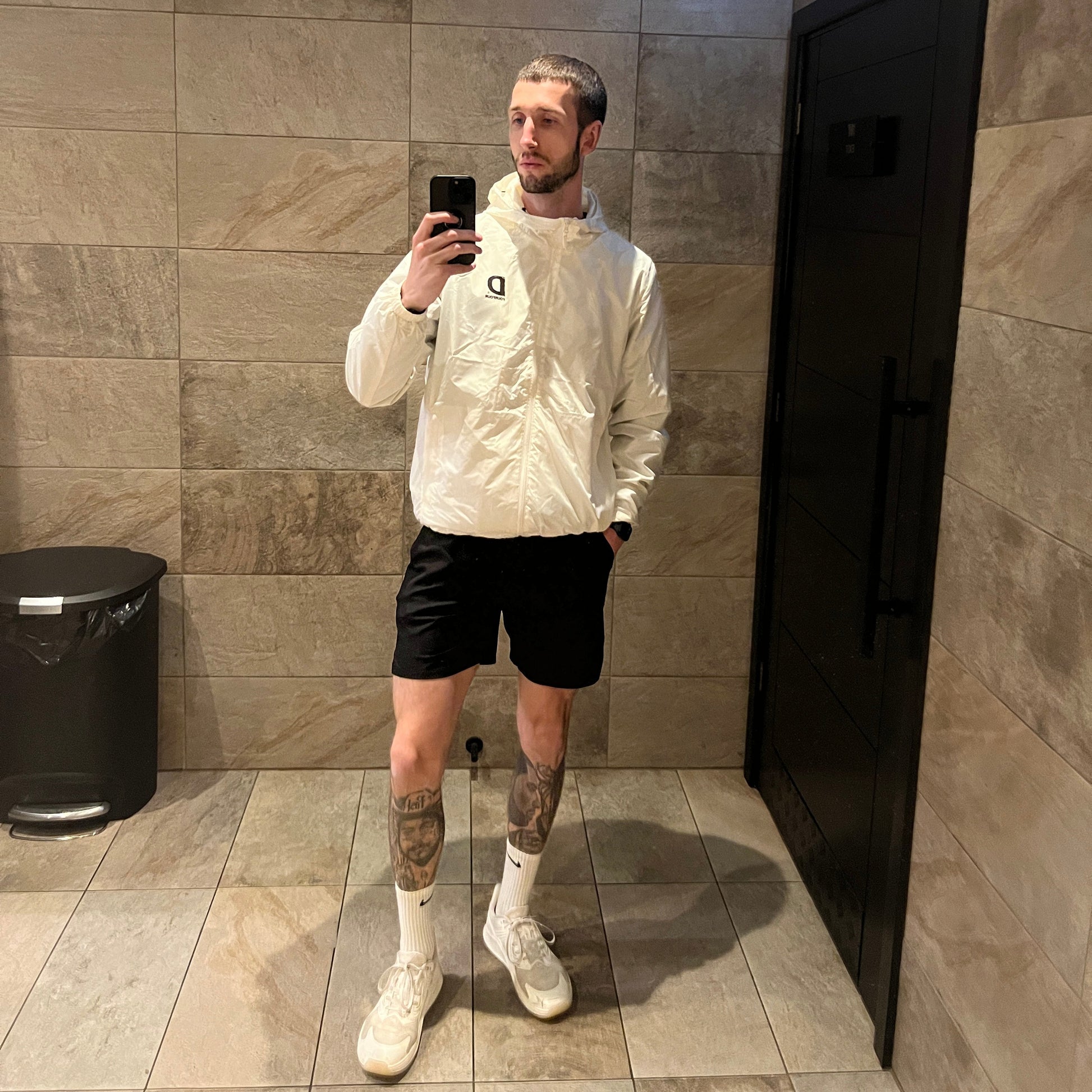 Person taking a mirror selfie in a bathroom with tiled floor and wall.