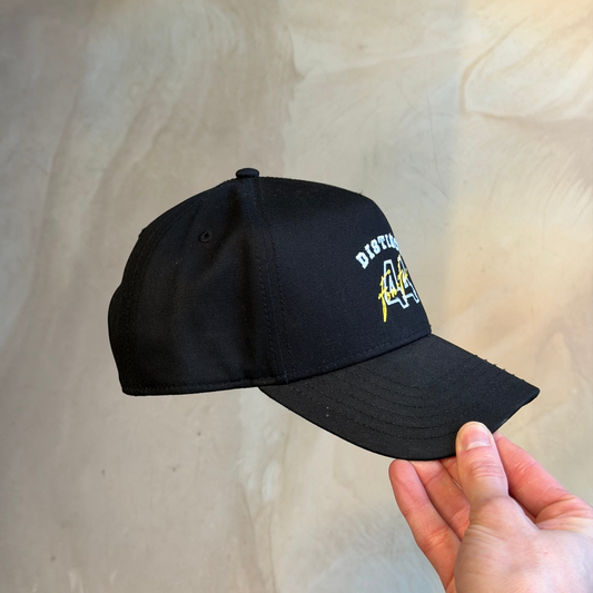 Black cap with logo held by a hand against a beige background