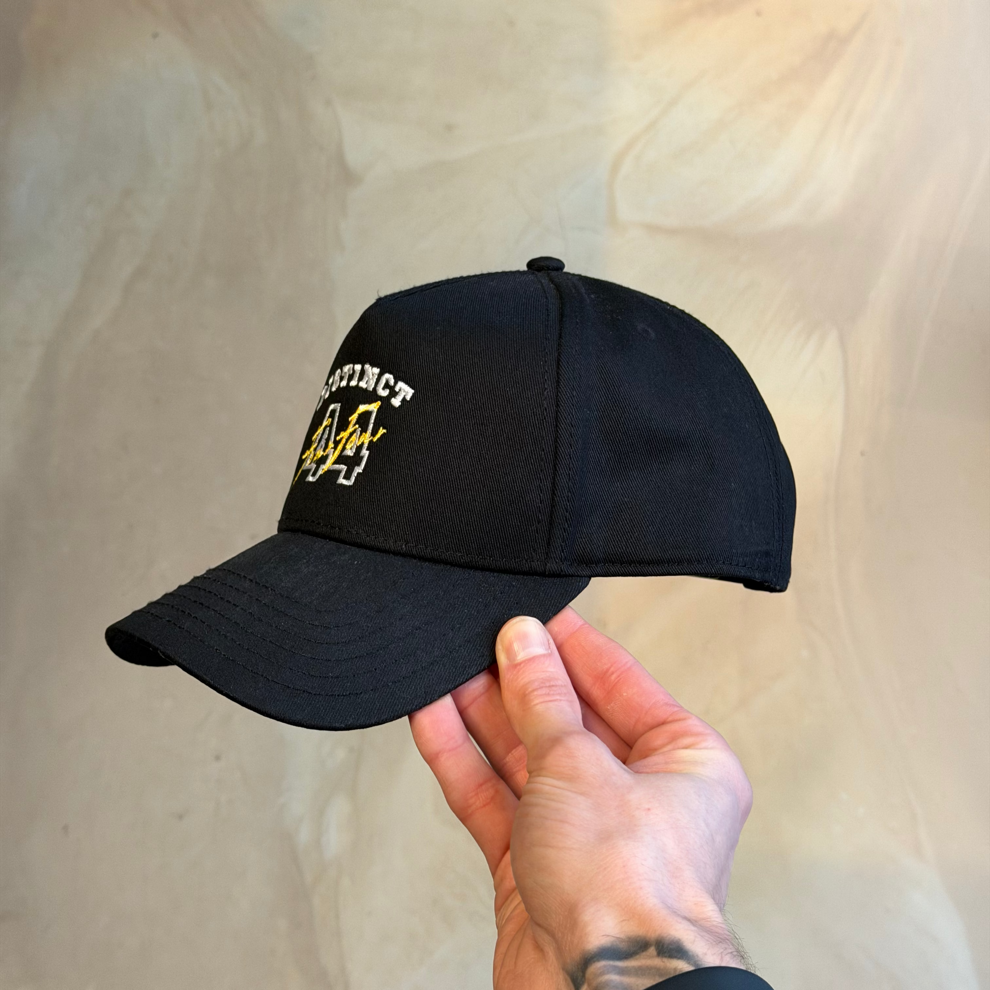 Black cap with yellow and white text held by a hand against a beige background