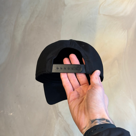 Black cap held by a hand against a neutral background