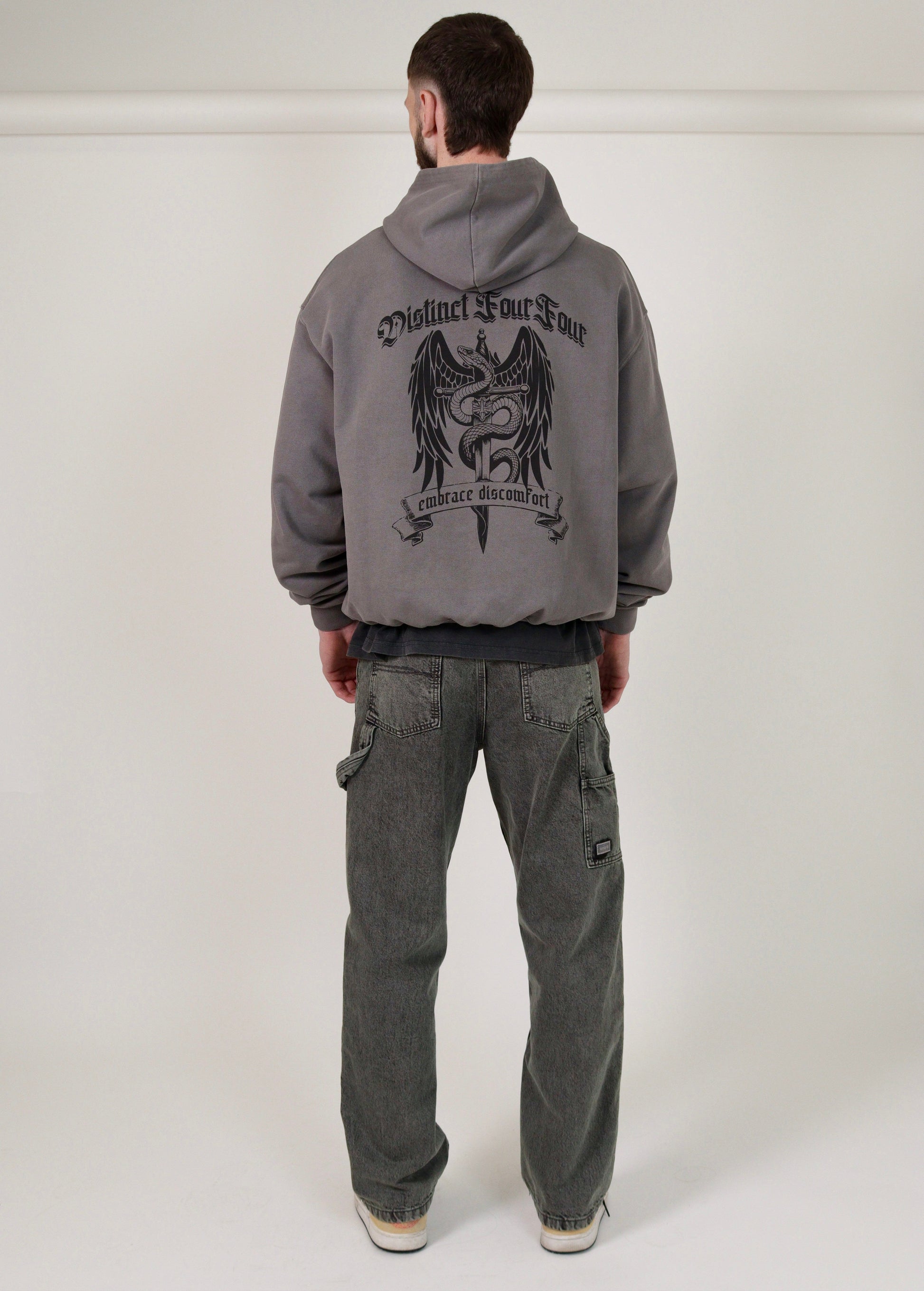 man wearing a grey hoodie with a graphic design on the back against a white background